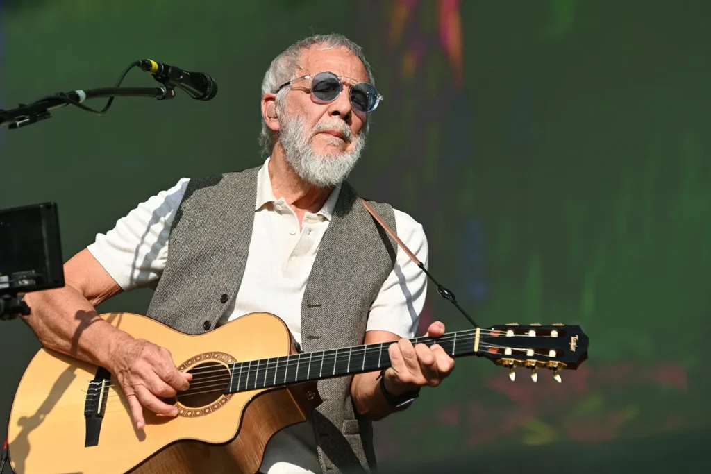 Cat Stevens, also known as Yusuf, has postponed the North American leg of his book tour due to unresolved visa issues, the singer confirmed on social media Monday. The Rock & Roll Hall of Fame inductee was scheduled to appear across the U.S. and Canada in support of his upcoming memoir, Cat on the Road to Findout. The book launches in the United States on October 7 after an earlier release in the U.K. Stevens reassured fans that the book release will remain unaffected, adding with humor: “Books don’t need visas!” Months of Delays and Rising Visa Costs Stevens explained that his team had been waiting months for visa approvals, but delays and increased fees made it impossible to finalize production logistics for the tour. “I am really upset! Not least for my fans who have bought tickets and made travel plans to see me perform,” Stevens wrote. He is the latest in a growing list of international musicians and athletes affected by slowed visa processing and rising application costs over the past year. Planned Tour Stops Affected The tour was slated to begin October 2 in Philadelphia and included multiple U.S. dates throughout the month. His October 8 Toronto stop was also postponed. The program was described as a “portal” into the singer’s world, combining in-depth conversations about his memoir with acoustic performances of selected songs. Stevens had already launched the book tour in the U.K. in September, visiting several cities. Possibility of Rescheduling While disappointed fans will need to wait, Stevens hinted the shows may be rescheduled if visas are approved in the future. However, new dates could be “some time away because of other travel plans.” He ended his message with an optimistic nod to one of his most famous songs, telling fans he hopes they can still “hop on the Peace Train route at some time in the future.”