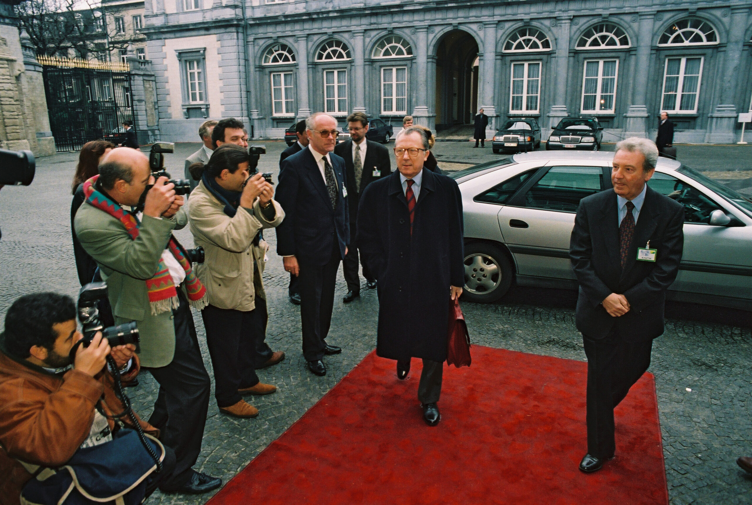 A European political leader addressing a group of officials with maps and documents visible on the table