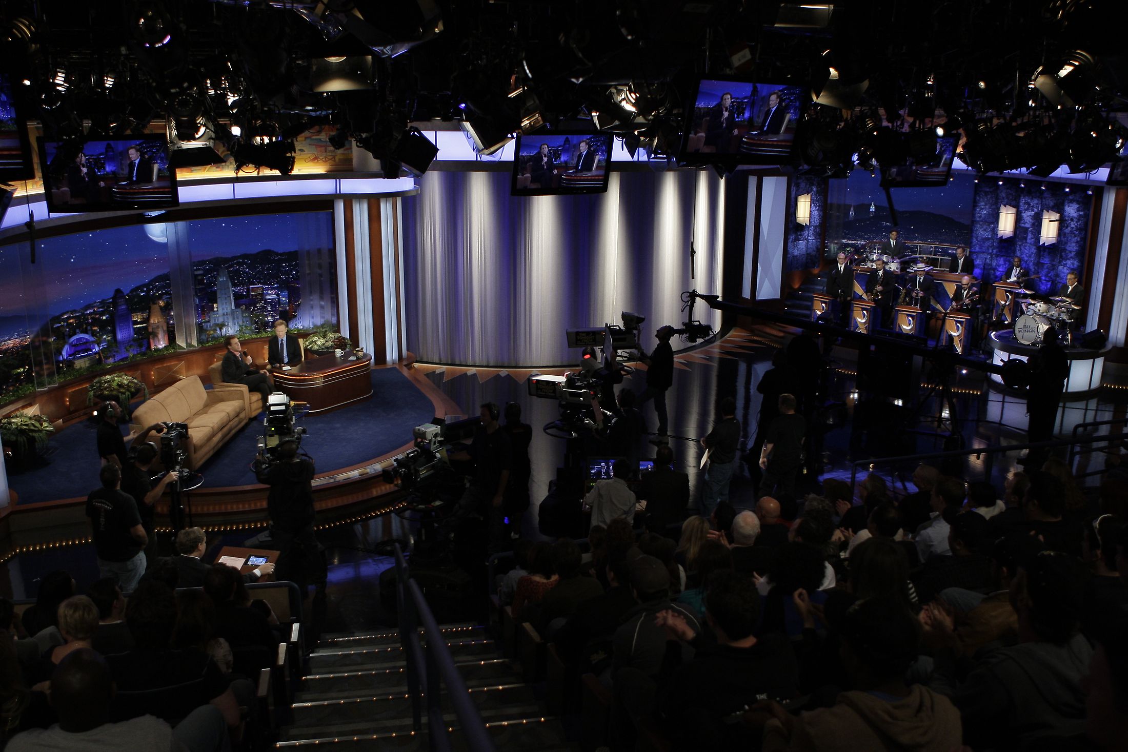 A late-night talk show host on set, engaging with an audience