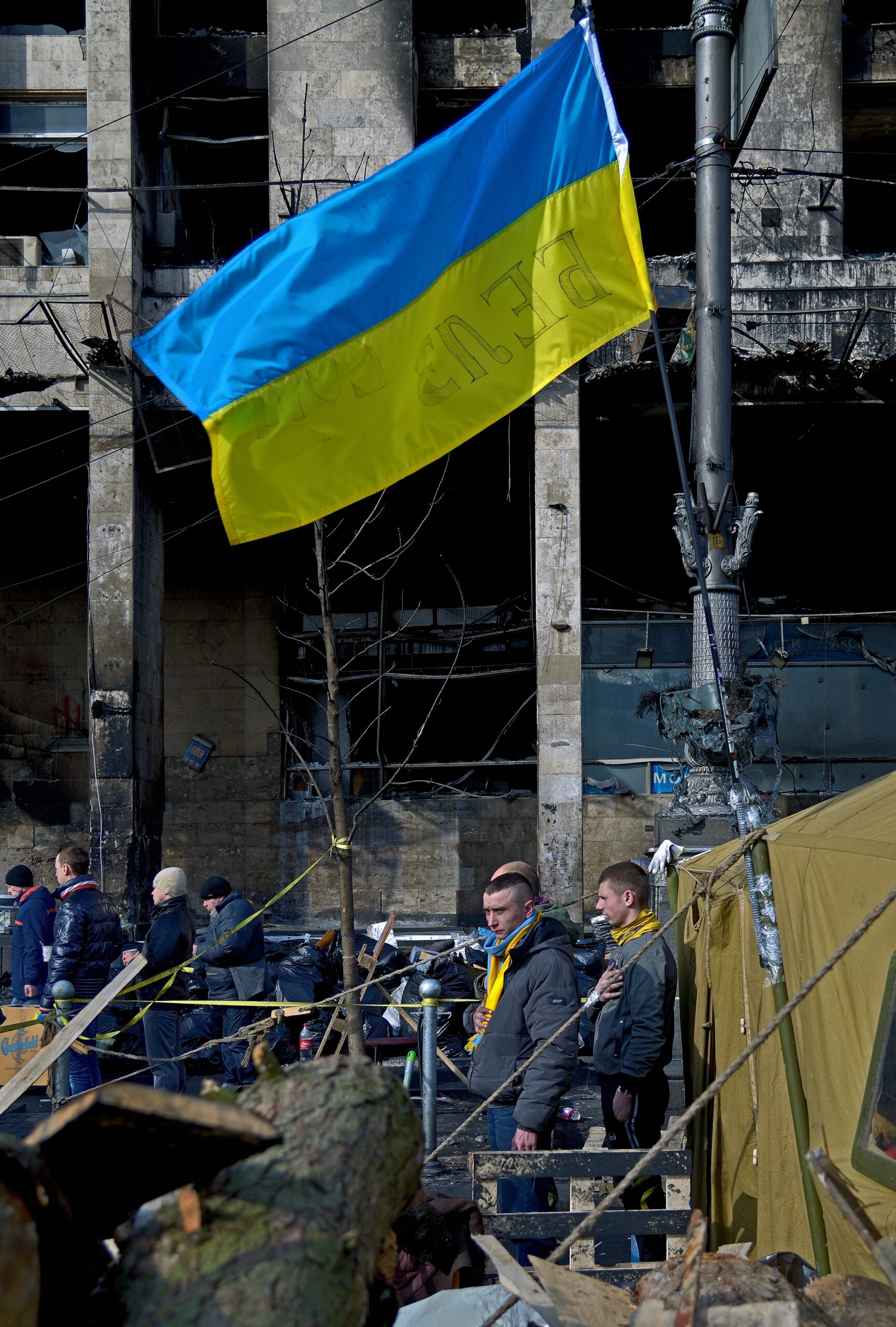 People waving Ukrainian flags near damaged infrastructure or a memorial site