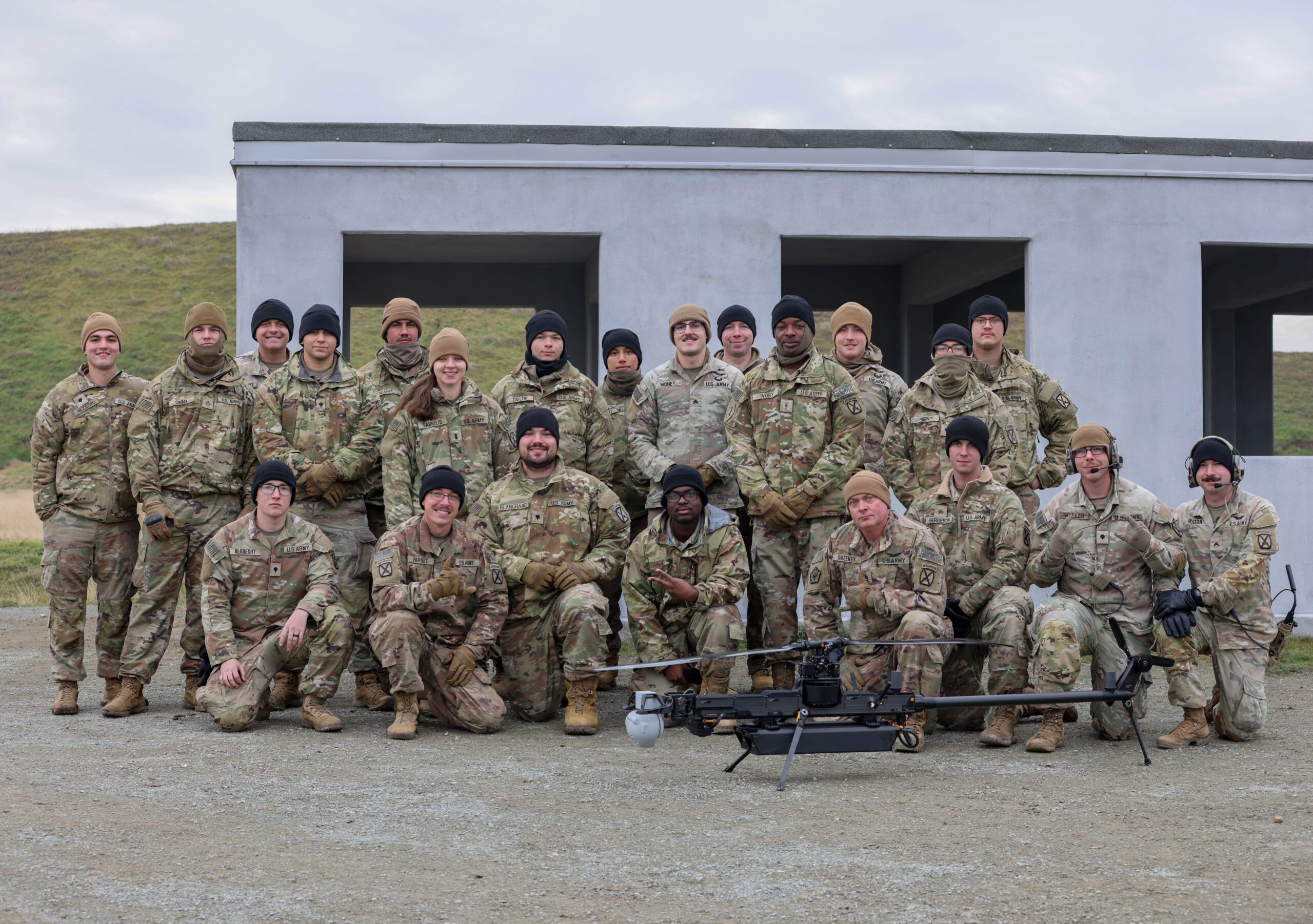 A soldier watching a drone fly overhead in an open field
