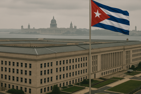 Cuban flag on a tall flagpole beside a large beige government building, with a domed capitol and distant skyline.