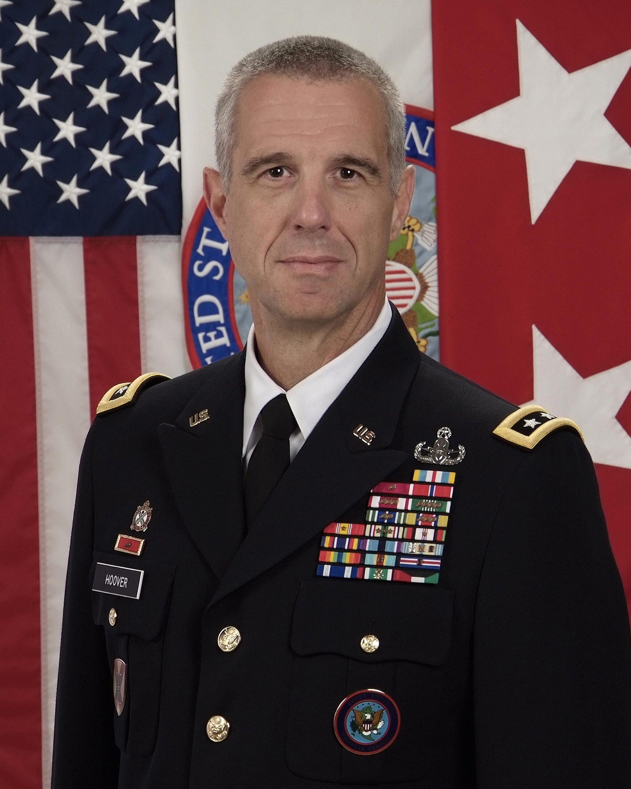 A high-ranking military official standing before an American flag, symbolizing leadership in the U.S. Army